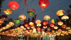 Chinese lanterns hung in rows by wires. The lanterns are light up agains the light sky.