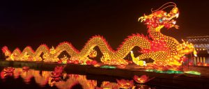 A Chinese dragon boat at night, lit up and reflected in the watre.